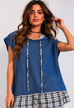 Woman wearing a blue sleeveless hoodie with plaid pants on a plain background